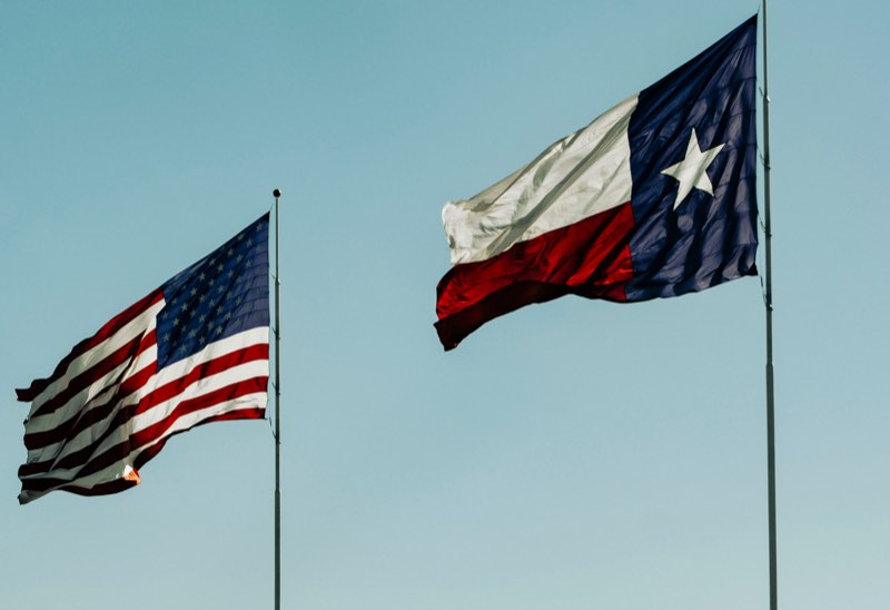 The Texas and American flags flying against a blue sky
